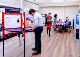 Voter standing at voting booth with second voter walking past in a vote center