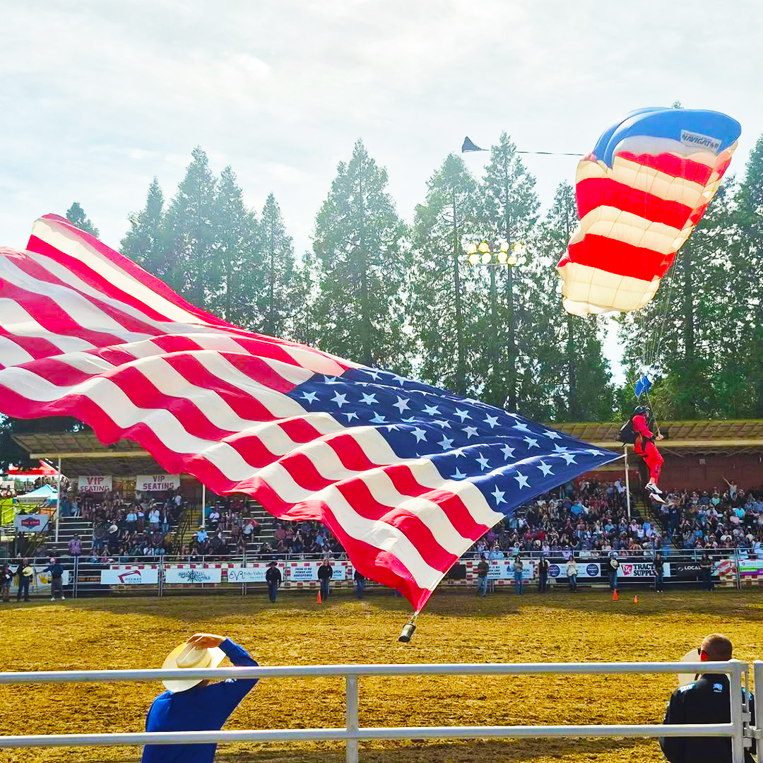 guy coming down with an american flag parachute on rodeo grounds