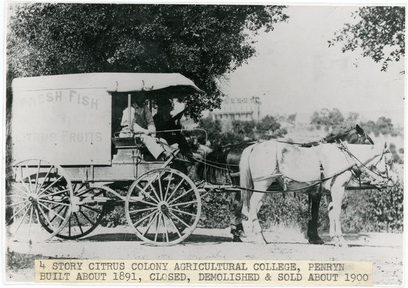 B&W photo of Two people sit in a canvas-covered wagon pulled by two horses.