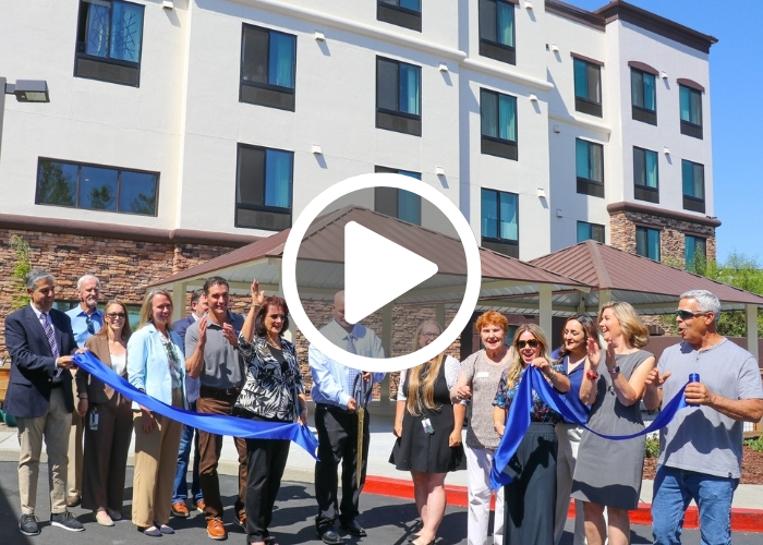 Group of folks stand in front of a large building cutting a blue ribbon