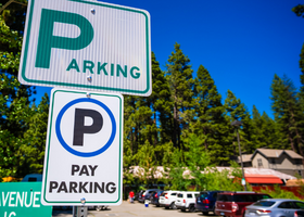 Two white parking and pay parking signs in a North Lake Tahoe lot full of cars
