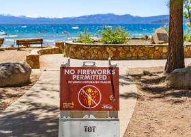 A ‘No fireworks permitted’ red sign at the beach access of Lake Tahoe and a yellow firework icon crossed out
