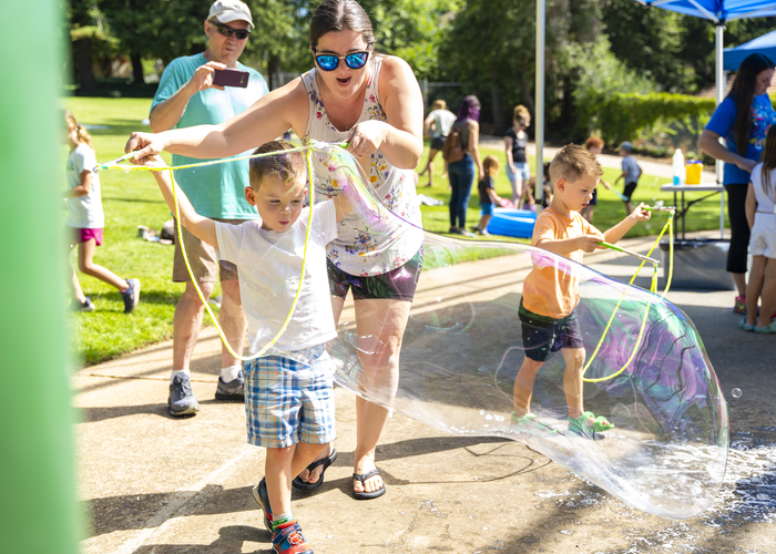 Two adults and two children play with large bubbles in a park