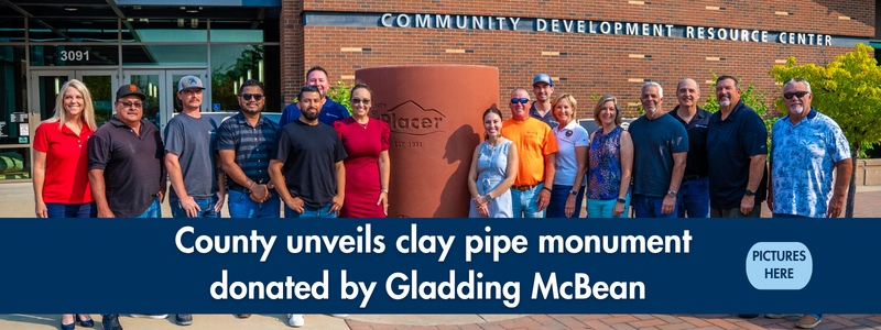 A clay pipe with the county logo engraved on it and 16 people posing for a group photo in front of a brick building