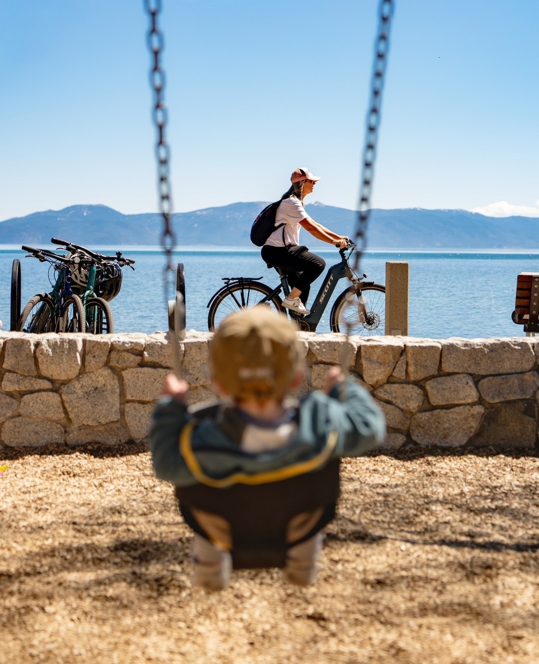 Photo of a kid on a swing facing the beach with a runner blurred in the background