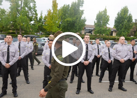 Law enforcement recruits stand at attention in shirts and ties as in instructor walks past them at the Placer County Sheriff Training Academy
