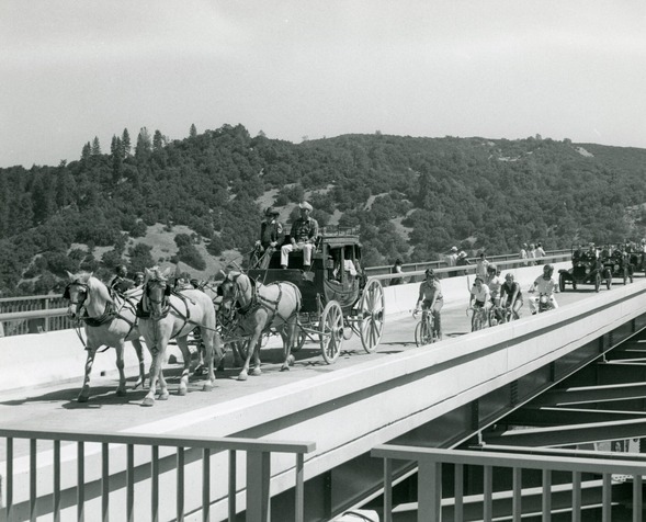 B&W photo of a horse carriage, cyclists and old cars on the Foresthill Bridge