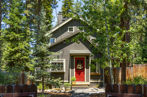 Grey home with a red door surrounded by green trees.