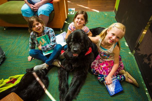 Black Labrador dog surrounded by 3 kids with books