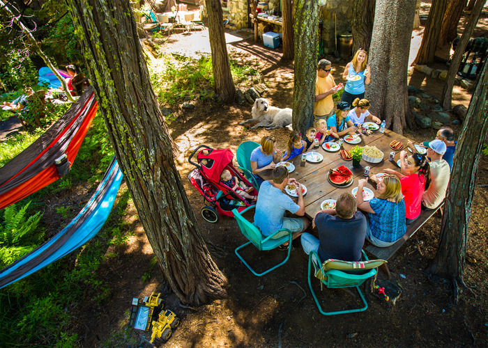 People eating at a camping trip, with hammocks in the trees nearby