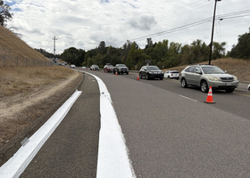 White line on shoulder of the road with cars going slow in the cone zone