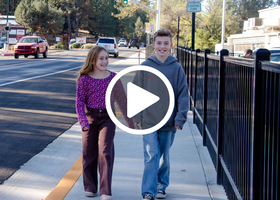 Two children walking on the new Meadow Vista Walkway near a black railing with a white play button overlay.