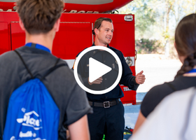 CAL FIRE/Placer County Fire Department employee speaking to students in front of a red truck at Youth in Government Day with a play button overlay.
