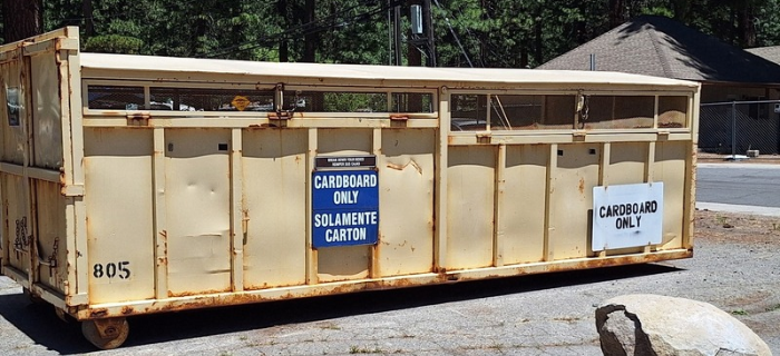 Tan recycling bin for cardboard only with signs in English and Spanish noting cardboard only.