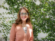 Woman in pink cardigan while standing in front of a white wall with leaves