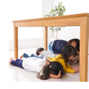 Four children practice covering their heads under a wooden table during an earthquake drill.