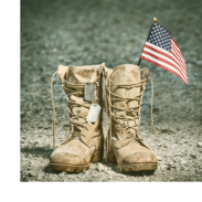 A dog tag and an American flag sit on top of combat boots.