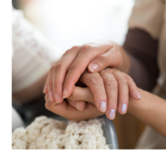 A caregiver wearing scrubs holds a woman's hands.