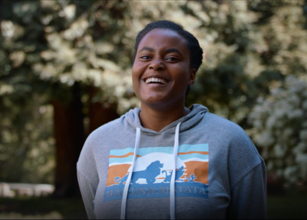 A young woman wearing stands outside and laughs.