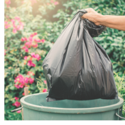 A hand throws a black trash bag into a green garbage can. 