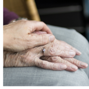 The hands of a senior sit in her lap. The hands of another senior are on top in a comforting gesture.