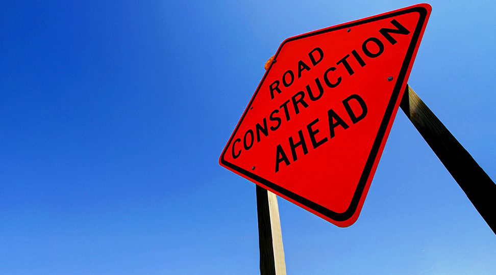 Road construction ahead sign, orange sign against blue sky