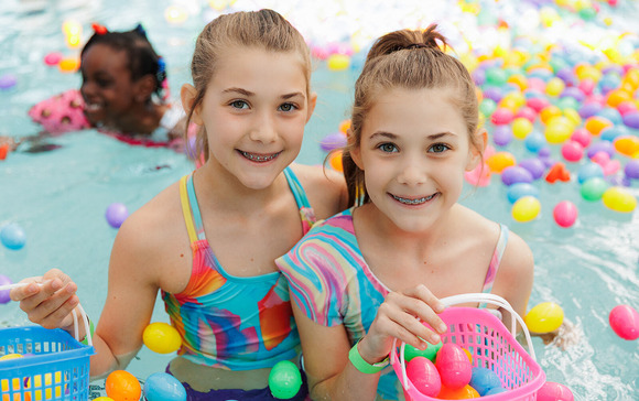 Photo of two girls smiling while swimming in a pool with floating Easter eggs