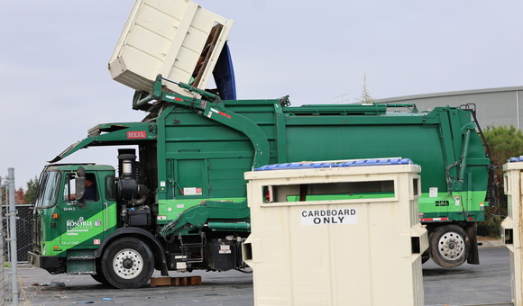 Photo of a trash truck picking up a dumpster bin, emptying the dumpster's contents into the body of the trash truck