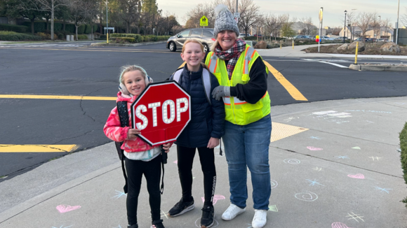 Group photo featuring two children holding a stop sign while smiling with their School Crossing Guard