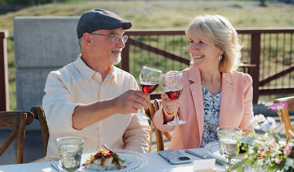 Photo of a couple smiling while toasting each others' wine glasses