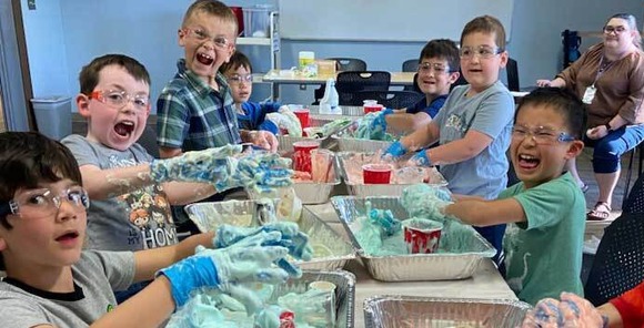 Photo of eight students and their teacher conducting an experiment with elephant toothpaste at a tab;e