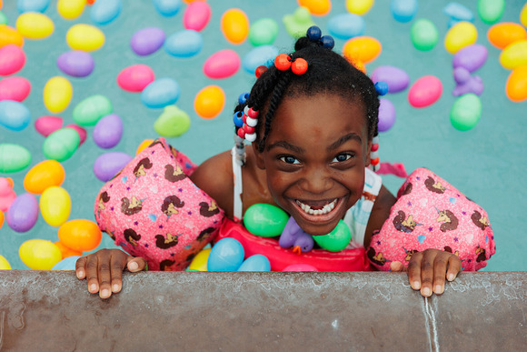 A little girl smiling while swimming in a pool filled with floating plastic eggs