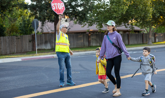 A crossing guard holds up a stop sign as a woman walks with two children across the crosswalk