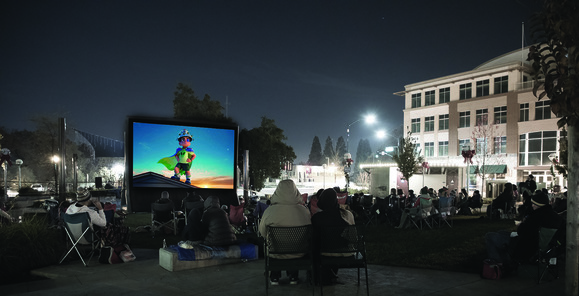 An audience sits in Vernon Street Town Square watching the movie, "Elio" on a large pop-up screen