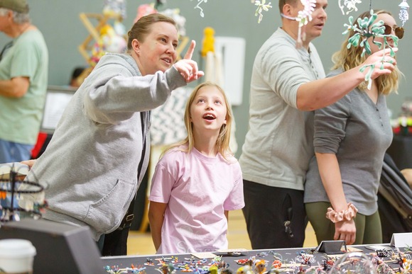 A smiling woman points at craft display as a young girl smiles and watches