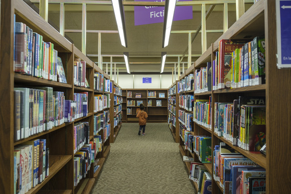 A child walks down the Downtown Library Children's Fiction aisle
