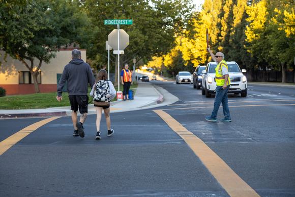 A parent and child on a crosswalk and a crossing guard holding up a Stop sign nearby