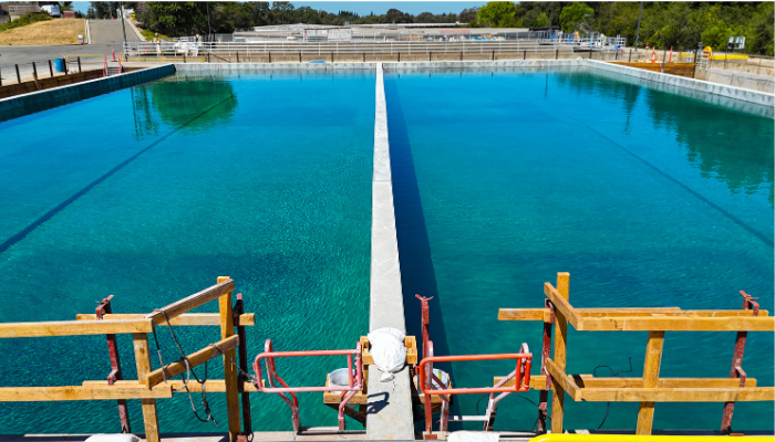 Two large, clear blue water basins divided by a concrete barrier, with construction scaffolding in the foreground