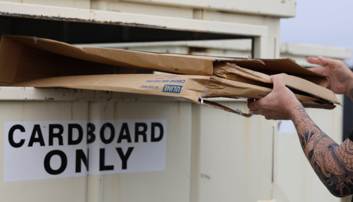 A person placing flattened cardboard into recycling bin