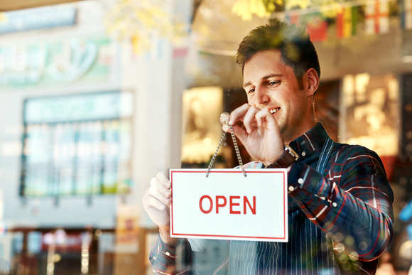 A smiling man places an open sign on the window of his business