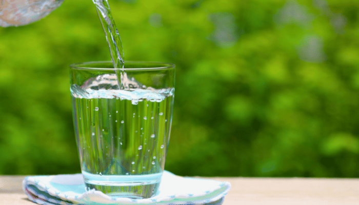 Clear water is being poured from a glass pitcher into a drinking glass, with bubbles forming in the water.