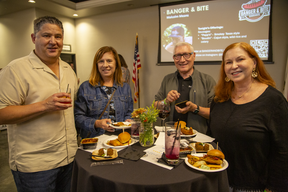 A group of four stands behind a table and smiles as they enjoy samples of the Roseville Rising Culinary showcase