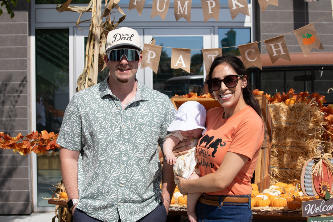 A woman and a man smile while holding their baby during the Family Fall Festival
