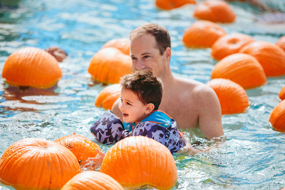 A father help his toddler swim in the floating pumpkin patch