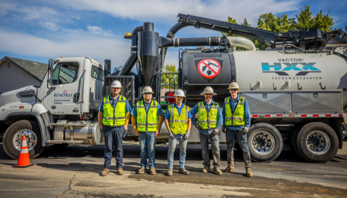 Construction crew standing in front of a large vacuum excavator truck