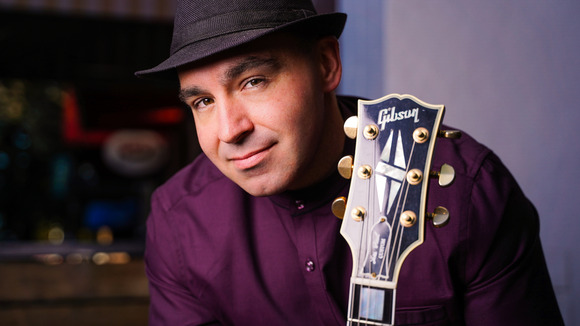 Paul Steward smiles while holding a guitar.