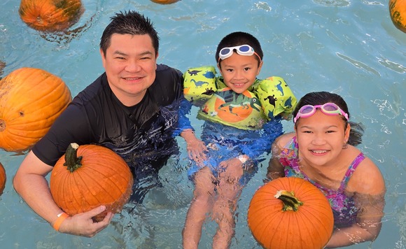 A man and two children from a pool as they hold pumpkins