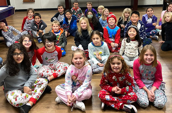 A group of children in pajamas smile while sitting on the floor.