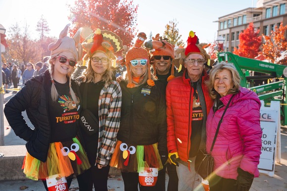 A family wearing Turkey Trot shirts smiles while standing in Vernon Street Town Square.