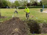 worker in yellow shirt digging a hole to access the irrigation system for repair